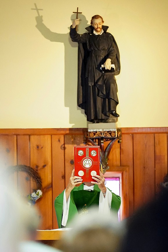 Father Robert Hohenstein stands in front of St. Isaac Jogues’s statue as he holds up the Book of Gospel during mass on Sunday, July 23, 2023, at St. Isaac Jogues Chapel, which is open from Memorial Day “til the snow flies,” in Saratoga Springs, N.Y.  Cindy Schultz for The Evangelist
