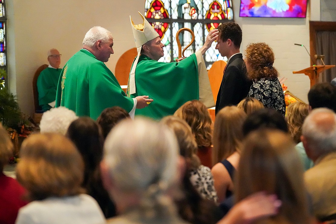 Bishop Edward B. Scharfenberger uses chrism to anoint candidate Josh Milone with sponsor Christine Santilli during confirmation on Oct. 29 at St. Kateri Tekakwitha Parish in Schenectady. At left, Father Bob Longobucco holds the chrism. (Cindy Schultz photo for The Evangelist)