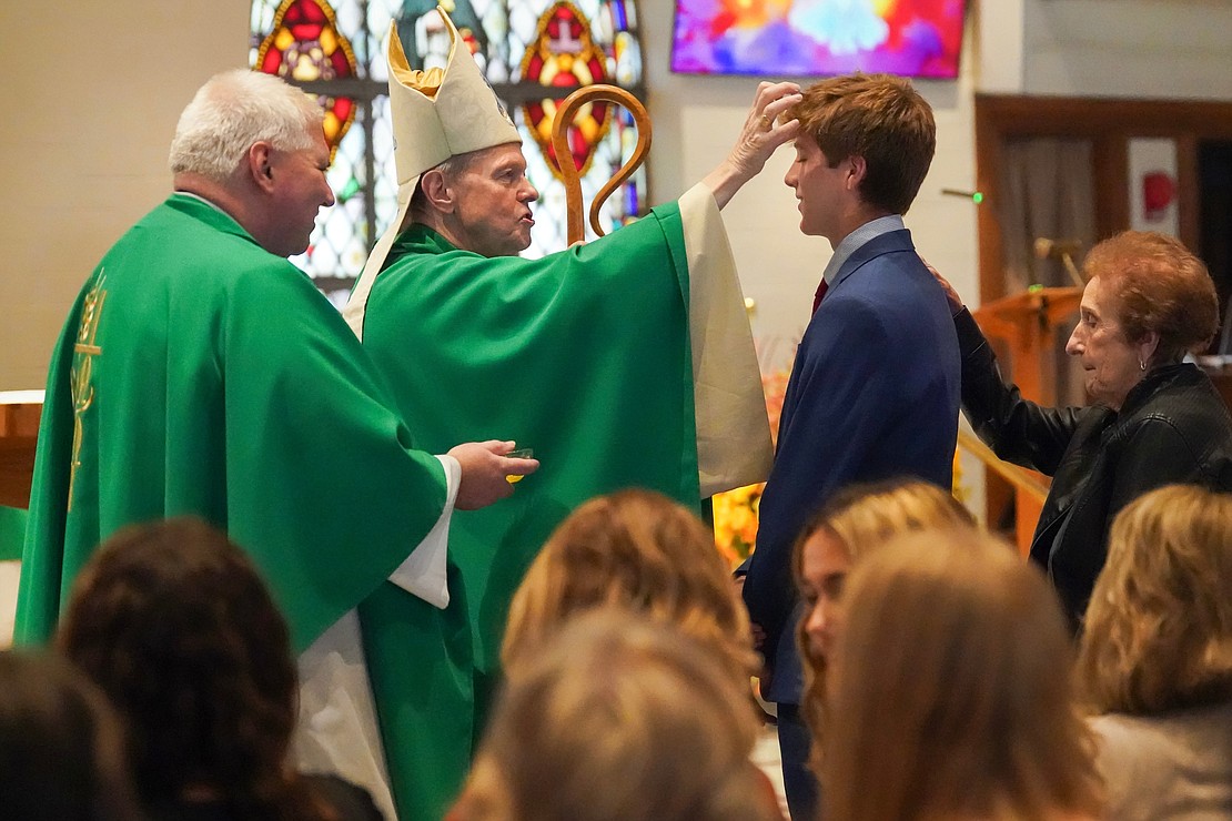 Bishop Edward B. Scharfenberger uses chrism to anoint candidate Eric Thurn with sponsor Mary Starsiak during confirmation on Oct. 29 at St. Kateri Tekakwitha Parish in Schenectady. At left, Father Bob Longobucco holds the chrism. (Cindy Schultz photo for The Evangelist)
