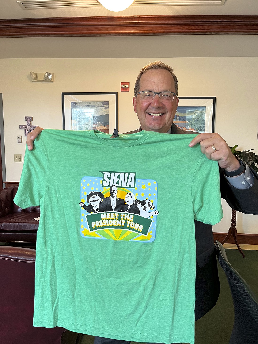 Dr. Charles Seifert, the first non-Catholic president of Siena College, holds up a t-shirt from his "Meet the President" tour to locations across the East Coast as Siena's newest president. The t-shirt design is a tribute to The Beatles' "Magical Mystery Tour" album and features Dr. Seifert and his wife, Deborah, Siena's mascot, and the college's official Saint Bernard, Baloo. (Emily Benson photo)