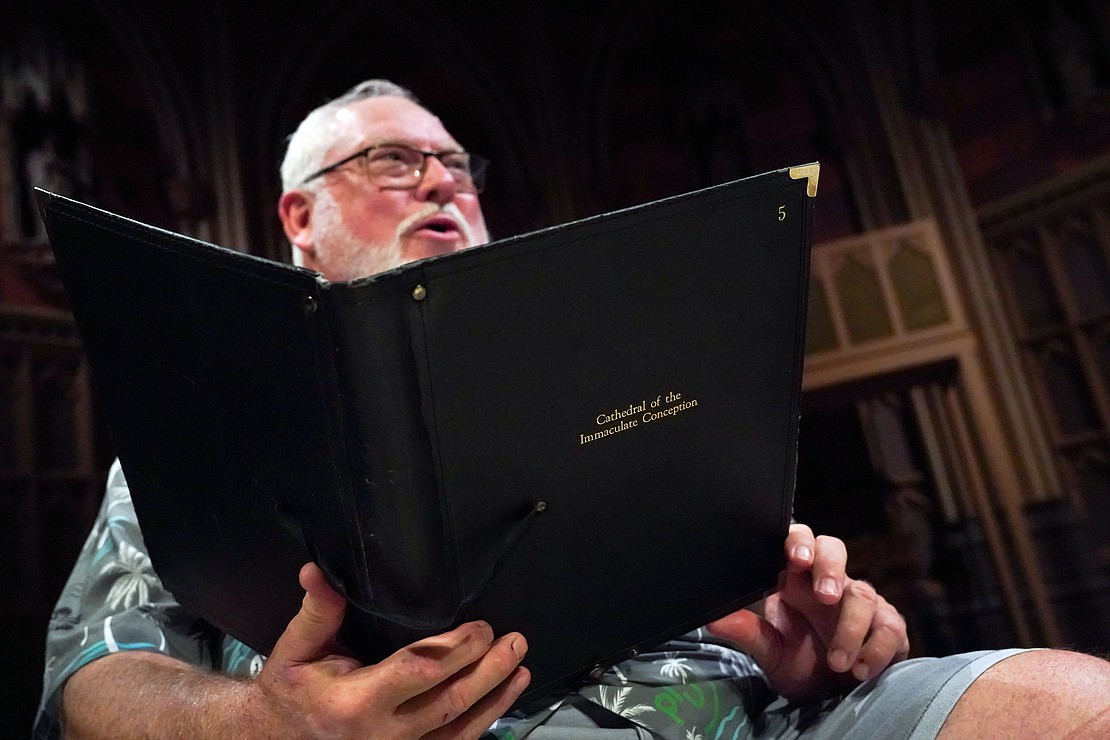 Tenor Bill Helmer refers to his notebook of songs during adult choir practice at the Cathedral of the Immaculate Conception in Albany. (Cindy Schultz photo for The Evangelist)