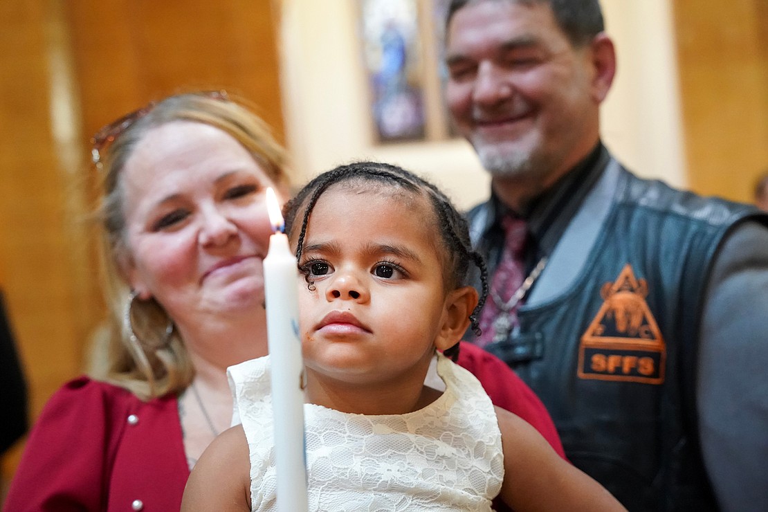 Londyn Raymond, 2, who is newly baptized, is with her godparents Starlette and C.J. Sheffield as they light a ceremonial candle at the conclusion of the ceremony on Sunday, Dec. 3, 2023, at Blessed Sacrament in Albany, N.Y.  Cindy Schultz for The Evangelist