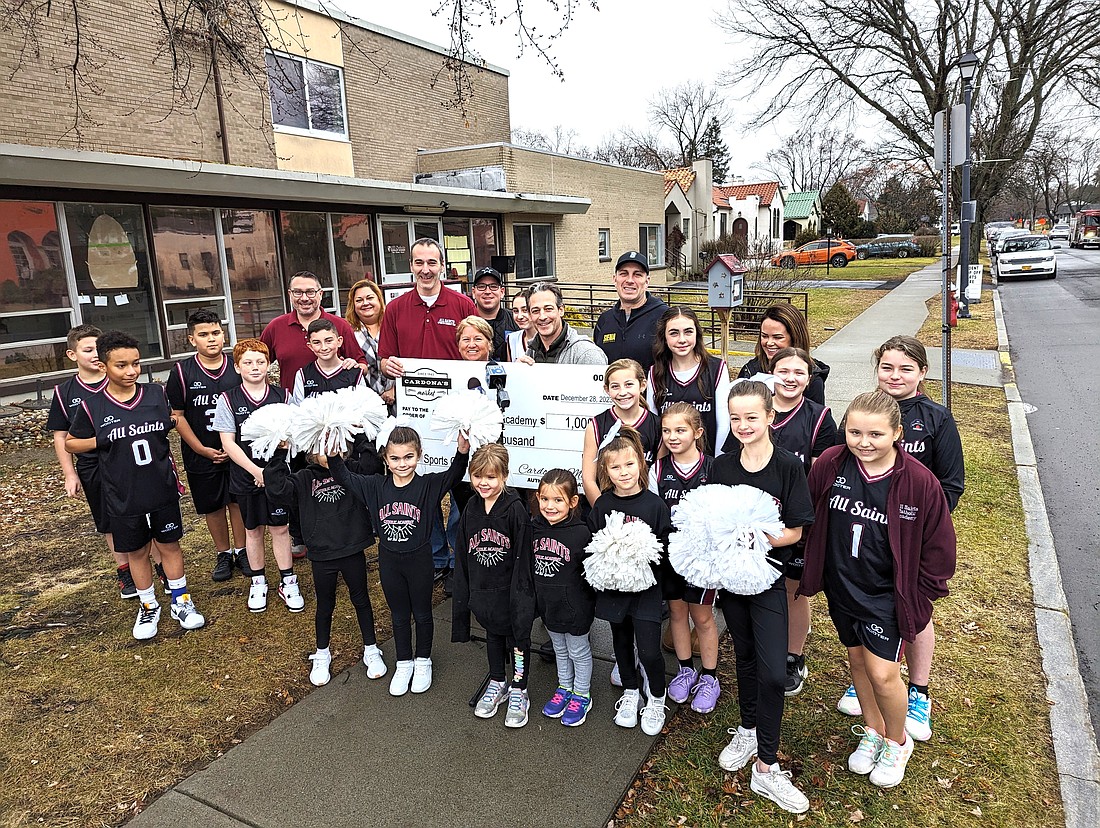 Members of the All Saints Academy basketball teams join Siena men’s basketball coach Carmen Maciariello (center far r., with Siena Jacket) and Cardona’s Market co-owner August Cardona (center with light-colored sweatshirt) who present a $1,000 check to Director of Albany CYO Michelle Vita (to Cardona’s right), and Director of Athletics at All Saints/Blessed Sacrament John Blanch (behind Vita) outside of All Saints Academy last month. (Photo provided)