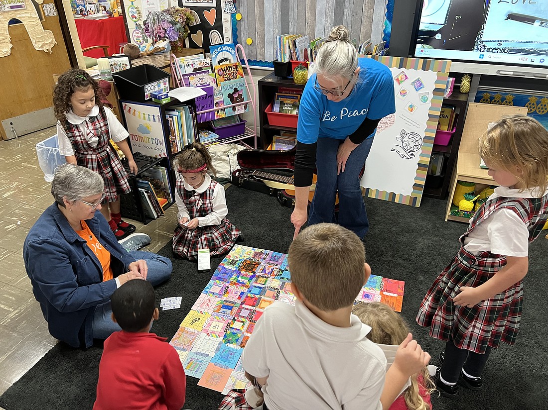 Sister Sue Zemgulis, OP, (l.), and Dr. Joy Galarneau help SMS kindergarteners put the quilt together, which was comprised of squares written with ways students can show love in action and held together with Band-Aids as a symbol for healing
through compassion. (Photos provided)