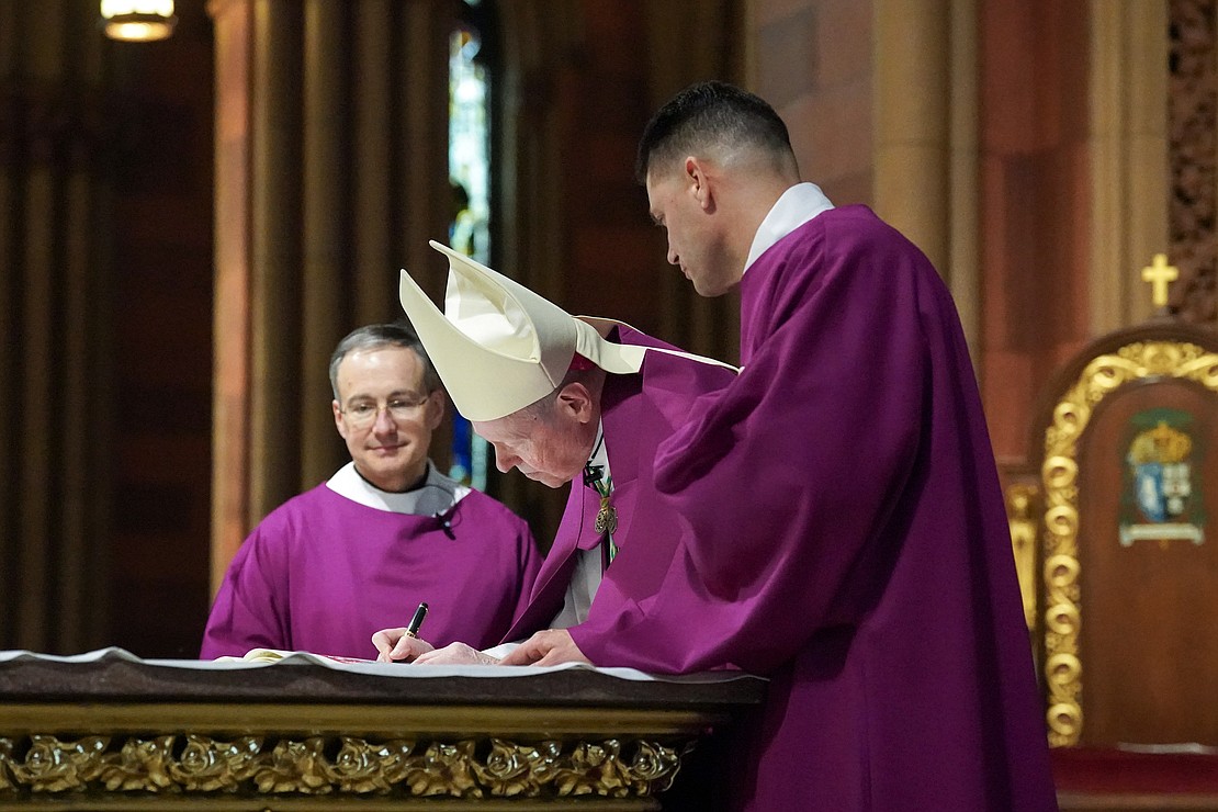 Bishop Edward B. Scharfenberger signs the Book of the Elect after catechumens register their names during the Rite of Election on Feb. 18 at the Cathedral of the Immaculate Conception in Albany. (Cindy Schultz photo for The Evangelist)