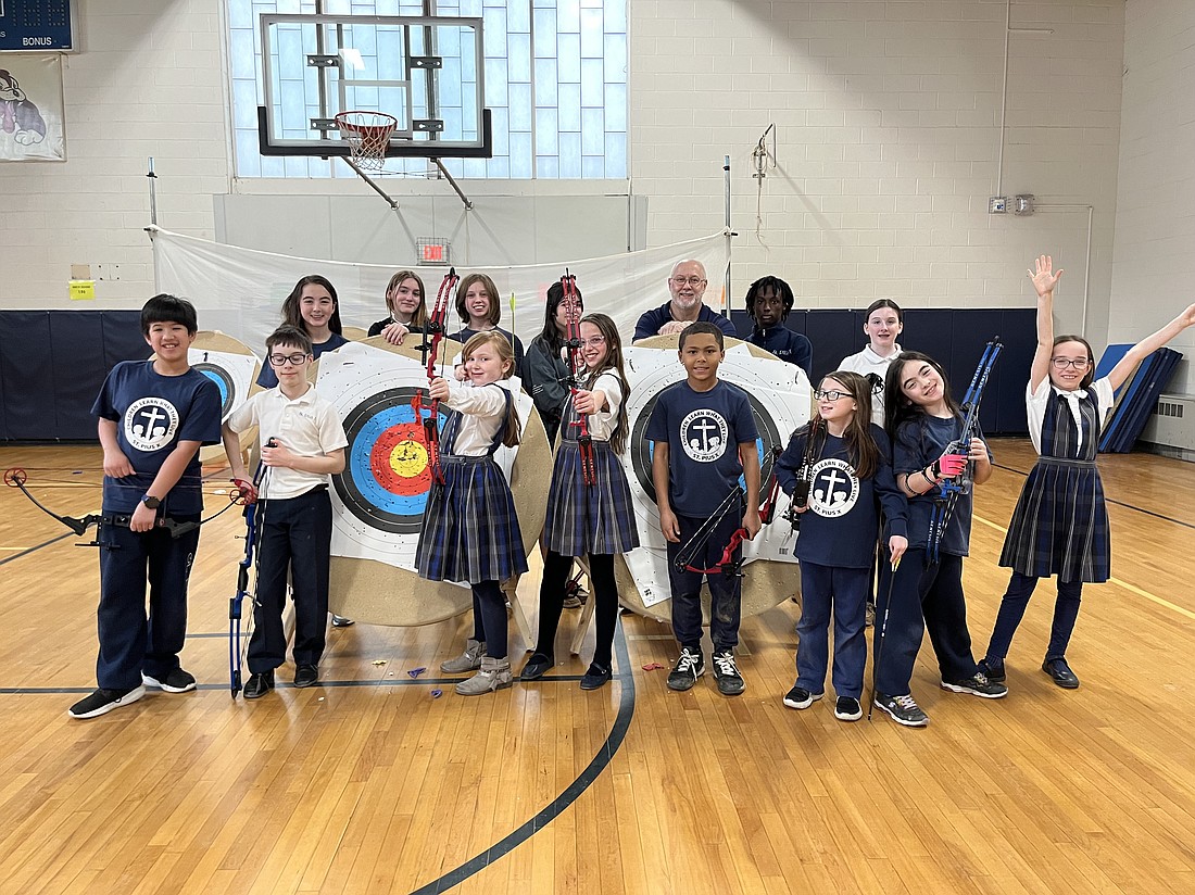 The St. Pius X archery club poses in front of their targets inside the school's gymnasium where practice is held on Tuesdays and Thursdays. (Emily Benson photo)