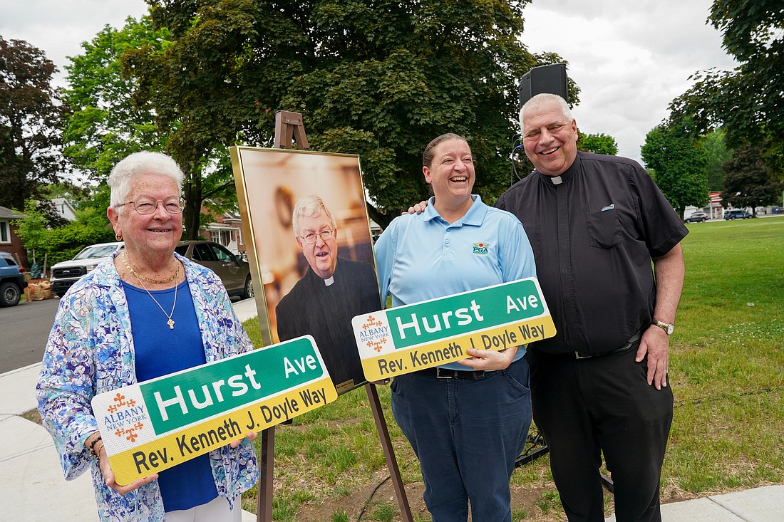 Mary Ellen Sochor, sister of Father Kenneth Doyle, left, and her niece Paula Sochor, center, hold replicas of the new street sign as they pose with Father Bob Longobucco and  Father Doyle’s portrait during the event to honor him on Tuesday, May 28, 2024, at Mater Christi Parish in Albany, N.Y.  Cindy Schultz for The Evangelist