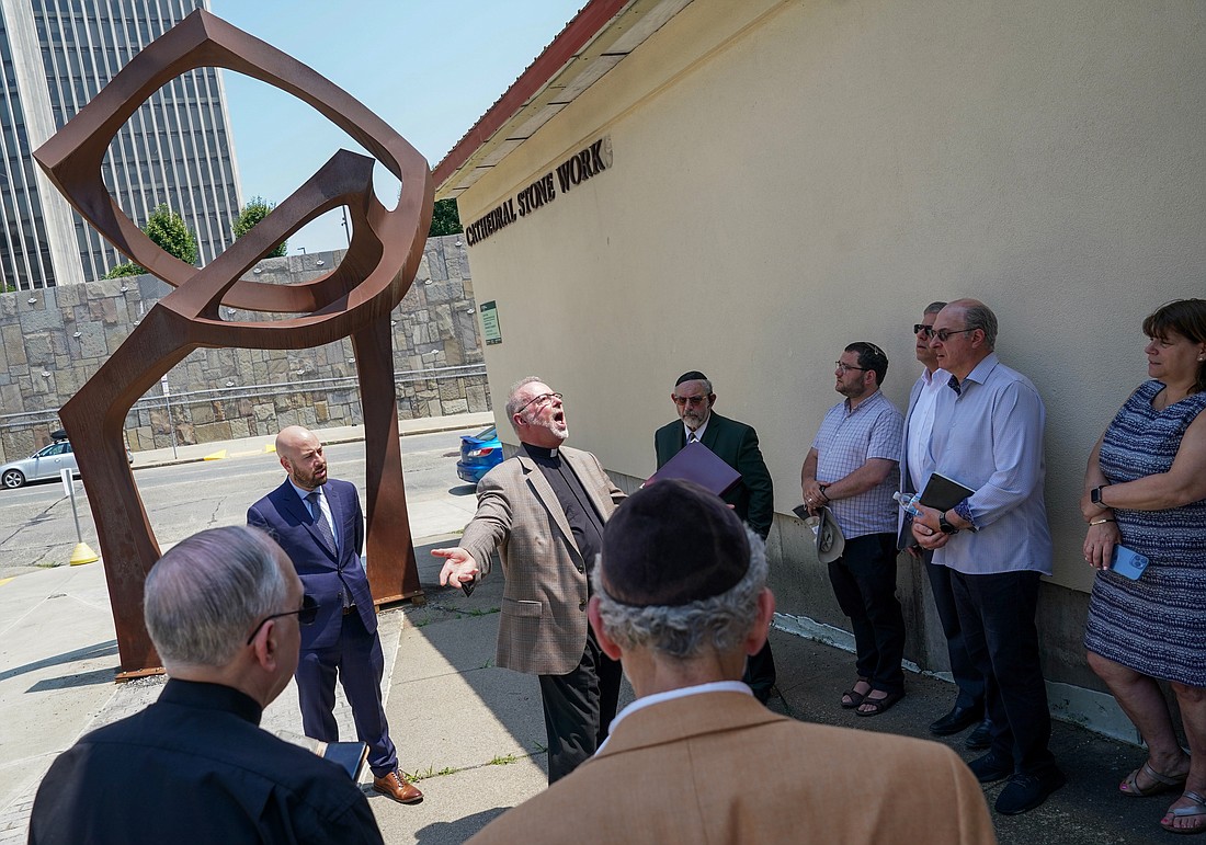 Father David Mickiewicz, center, leads a song in front of The Portal sculpture on Friday, June 21, 2024, at the Cathedral of Immaculate Conception in Albany, N.Y. The event, which included prayers and singing, recreated the sculpture’s dedication. The Portal represents forgiveness between Christians and Jews.  Cindy Schultz for The Evangelist