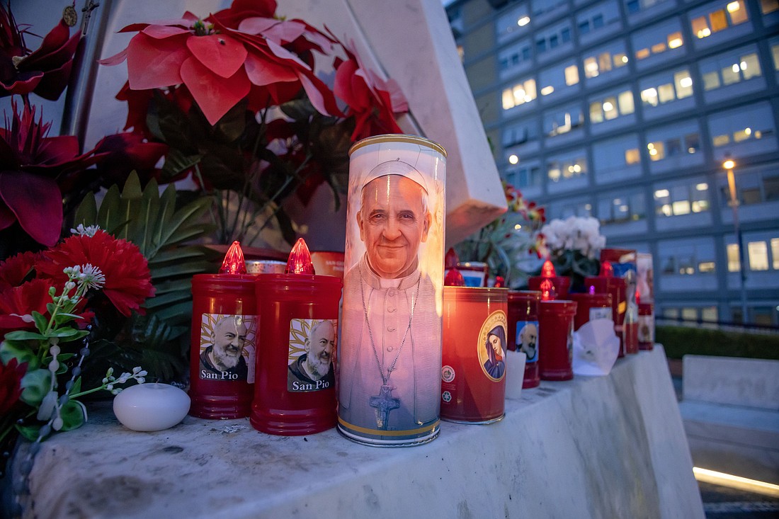 Votive candles and flowers are seen at the base of a statue of St. John Paul II outside Rome's Gemelli hospital Feb. 19, 2025, where Pope Francis is being treated for double pneumonia. (CNS photo/Pablo Esparza)