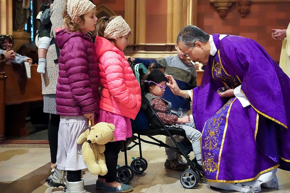 Father Rendell Torres places ashes on the forehead of one of Cheryl DePra’s children  during Ash Wednesday Mass on March 5 at the Cathedral of the Immaculate Conception in Albany. (Cindy Schultz photo for The Evangelist)