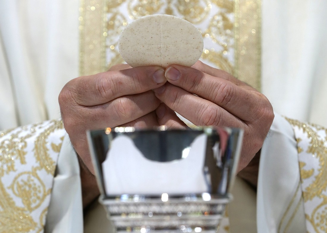 A priest holds the Eucharist in this photo illustration. (OSV News photo/CNS file, Bob Roller)