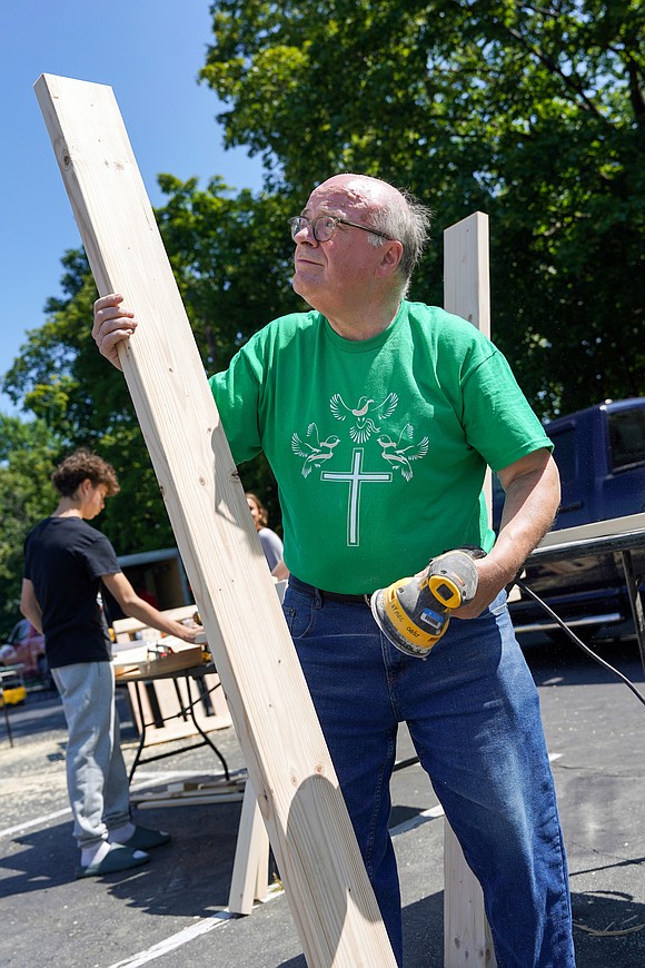 Father Joseph O’Brien looks over a plank while sanding it as part of the Sleep in Heavenly Peace project on Aug. 2 at St. Michael the Archangel Church in Troy. Parishioners and volunteers assembled headboards, footboards and sideboards needed to make bed frames for children. (Cindy Schultz photo for The Evangelist)