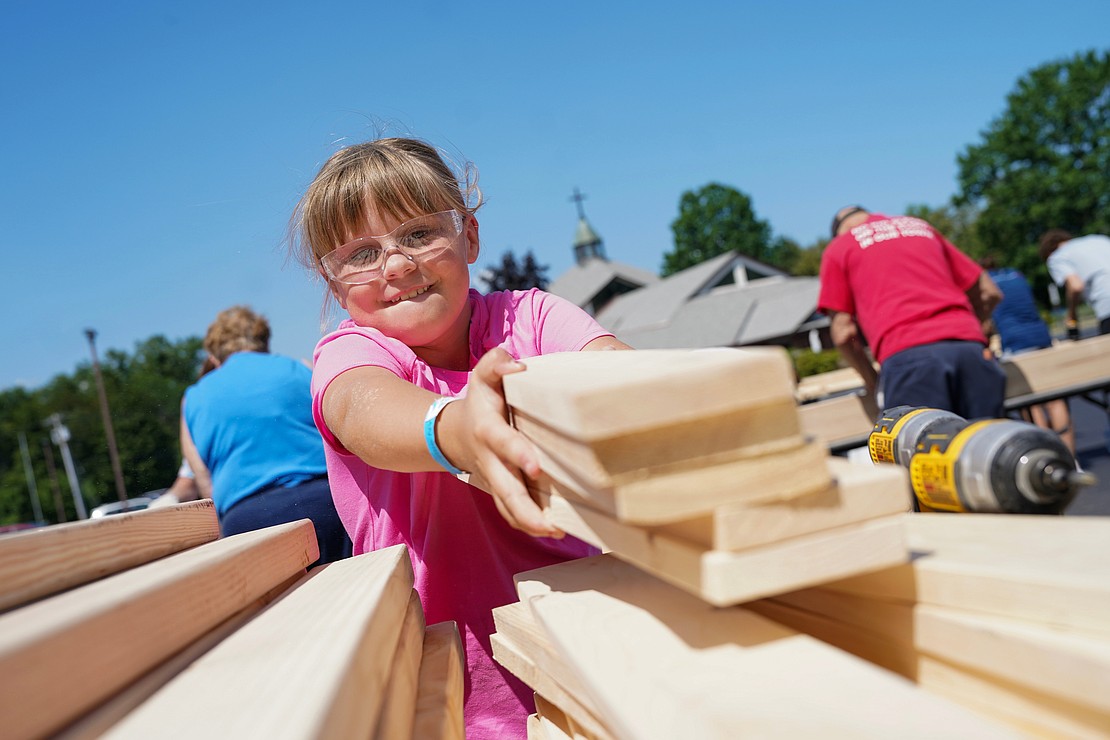 Kaleigh Ublacker, 7, helps move wood planks to the next station as part of the Sleep in Heavenly Peace project on Aug. 2 at St. Michael the Archangel Church in Troy. Parishioners and volunteers assembled headboards, footboards and sideboards needed to make bed frames for children. (Cindy Schultz photo for The Evangelist)