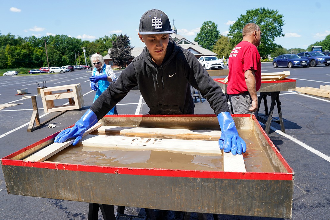 Braydon Huestis, 14, soaks bed frame pieces in a vinegar mixture to preserve the wood and prevent insect damage as part of the Sleep in Heavenly Peace project on Aug. 2 at St. Michael the Archangel Church in Troy. Parishioners and volunteers assembled headboards, footboards and sideboards needed to make bed frames for children. (Cindy Schultz photo for The Evangelist)