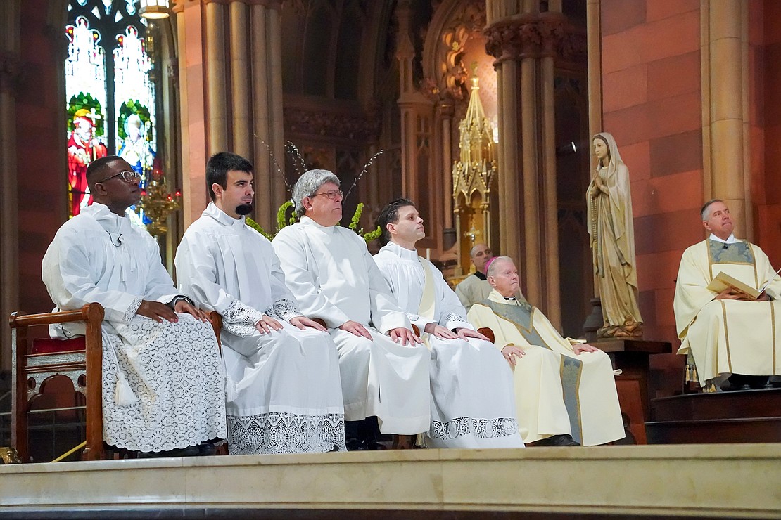 Gilbert Kimaro (from l.), Alessio Fasullo, and Timothy Kilpeck, deacons candidates, Alexander Turpin, candidate for the priesthood and sitting next to Bishop Emeritus Edward B. Scharfenberger)=, listen to Bishop Mark O’Connell’s homily during the Mass of Ordination to the Priesthood and the Diaconate on May 16 at the Cathedral of the Immaculate Conception in Albany. (Cindy Schultz photo for The Evangelist)