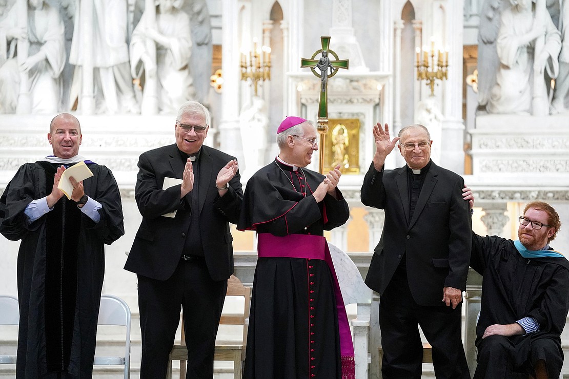 Father Leo Markert (second from r.) acknowledges the audience as they sing happy birthday to mark his 90th birthday during the Notre Dame-Bishop Gibbons commencement exercises on June 6 at St. John the Evangelist in Schenectady. Joining him (from l.) are Superintendent of Schools Christopher Bott, Father Bob Longobucco, Bishop Mark O’Connell and school counselor Samuel South. (Cindy Schultz photo for The Evangelist)