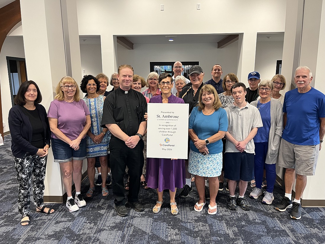 Renee Hallock (far l.), point person for the St. Ambrose CarePortal, Father Brian Kelly, pastor, and dozens of St. Ambrose CarePortal responders are presented with an award from Trisha Gerstel (c. with sign), regional manager for Justice for Orphans, marking the parish’s milestone of helping 1,000 children in need. (Emily Benson photo)