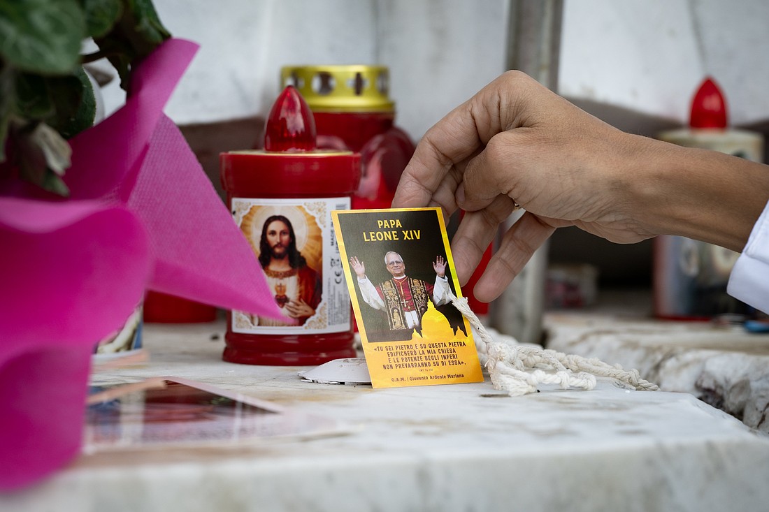 A woman touches some devotional items placed next to a statue of St. John Paul II Oct. 14, 2026, in front of Rome's Gemelli hospital where Pope Leo XIV is recovering from surgery during which doctors removed his lower right lung to treat a cancerous tumor. (CNS photo/Cristian Gennari)
