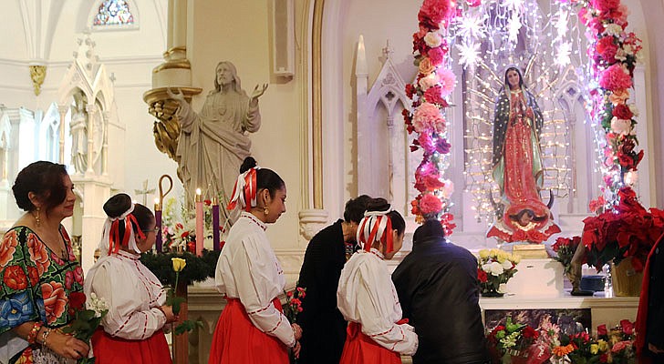 The Shrine Church of Our Lady of the Americas in Albany celebrated a Mass honoring Our Lady of Guadalupe with Bishop Edward B. Scharfenberger on Sunday, Dec. 15. According to CNS, “Our Lady of Guadalupe appeared to St. Juan Diego on Tepeyac Hill near Mexico City on Dec. 9 and Dec. 12, 1531, saying she wanted a church built in her honor on that hill. The bishop, who originally ignored Juan Diego, asked for a sign from her and Mary produced enough roses in December to fill his tilma, a type of outer garment. When he emptied the cloak and the roses fell in front of the bishop, he found that she had left her image on the cloak, which remains today in the Basilica of Our Lady of Guadalupe in Mexico City.” The feast day of Our Lady of Guadalupe is Dec. 12.   Worshippers at the Shrine Church of the Americas place flowers at the base of the statue of Our Lady of Guadalupe. The service is traditionally held on the third Sunday of Advent.  Photos by Thomas Killips