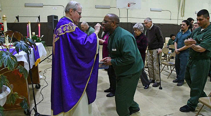 Bishop Edward B. Scharfenberger celebrated a special Christmas Mass for inmates at the Washington Correctional Facility in Comstock on Thursday, Dec. 19. Deacon Miguel Fabian, the facility’s chaplain, Father Rendell Torres and Deacon Ryan McNulty resided over the Mass, which was held in the facility’s gymnasium and attended by 33 inmates.  Bishop Scharfenberger (clockwise from top) delivers his homily, “Opening one’s Heart to Jesus”; one inmate holds a bible; another man prays; and a cross is creatively attached to the rim of the gym’s basketball hoop.  Bishop Scharfenberger distributes Communion.  Michael P. Farrell photos