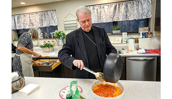 Bishop Edward B. Scharfenberger pours marinara sauce over butternut squash noodles during a Kitchen Wisdom cooking class at the Family Life Center on Feb. 22 at the City Mission in Schenectady The women who live at the center were learning to make butternut squash noodles and marinara sauce.    Cindy Schultz photo for The Evangelist